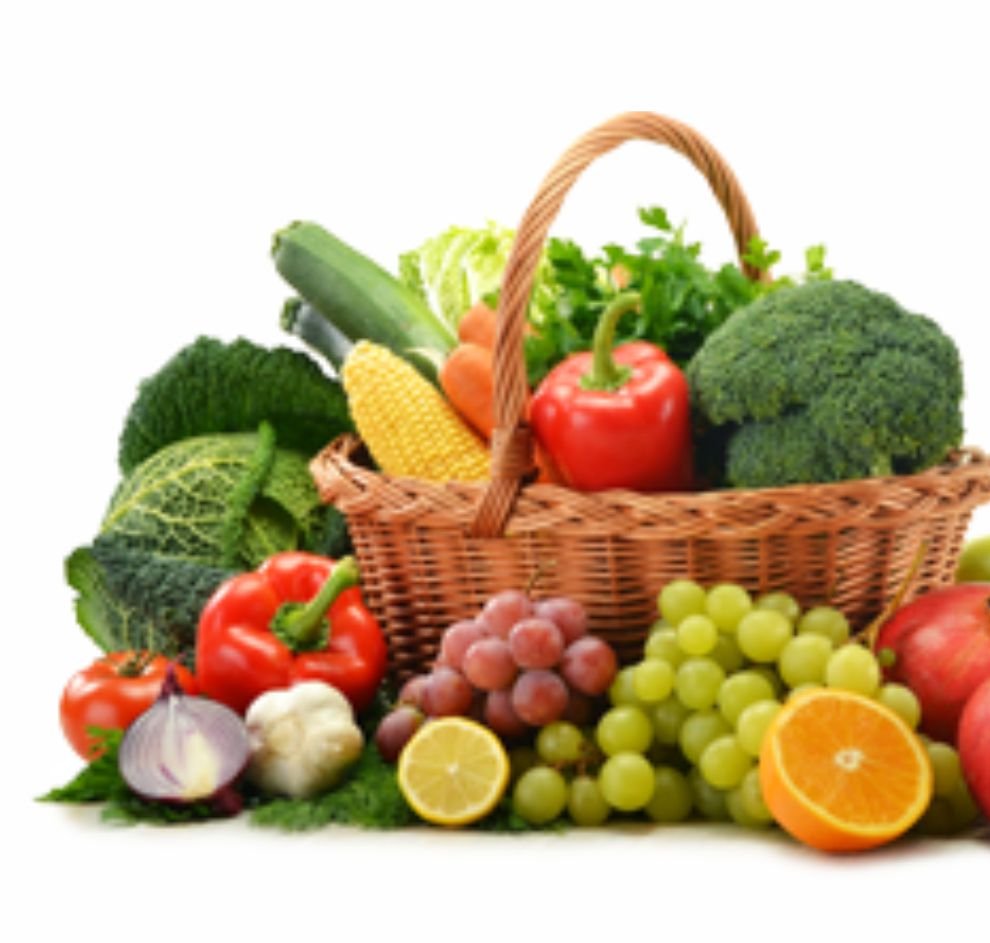 Cesta de vime com abobrinha, milho, cenoura, pimentão, brócolis e folhas verdes, cercada de repolho, tomate, cebola, alho, uvas, limão, laranja e maçã, sobre fundo branco