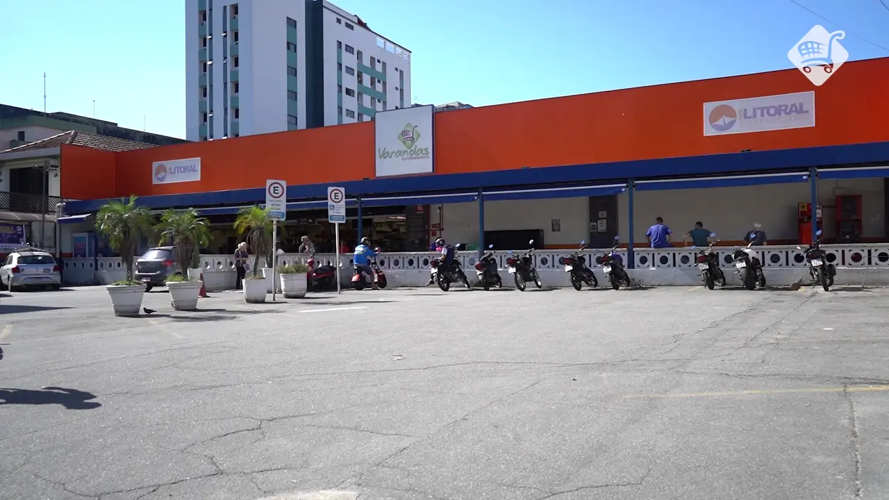 Fachada laranja de uma loja do Supermercado Varandas, com os letreiros do Varandas e da Rede Litoral e motos estacionadas em frente